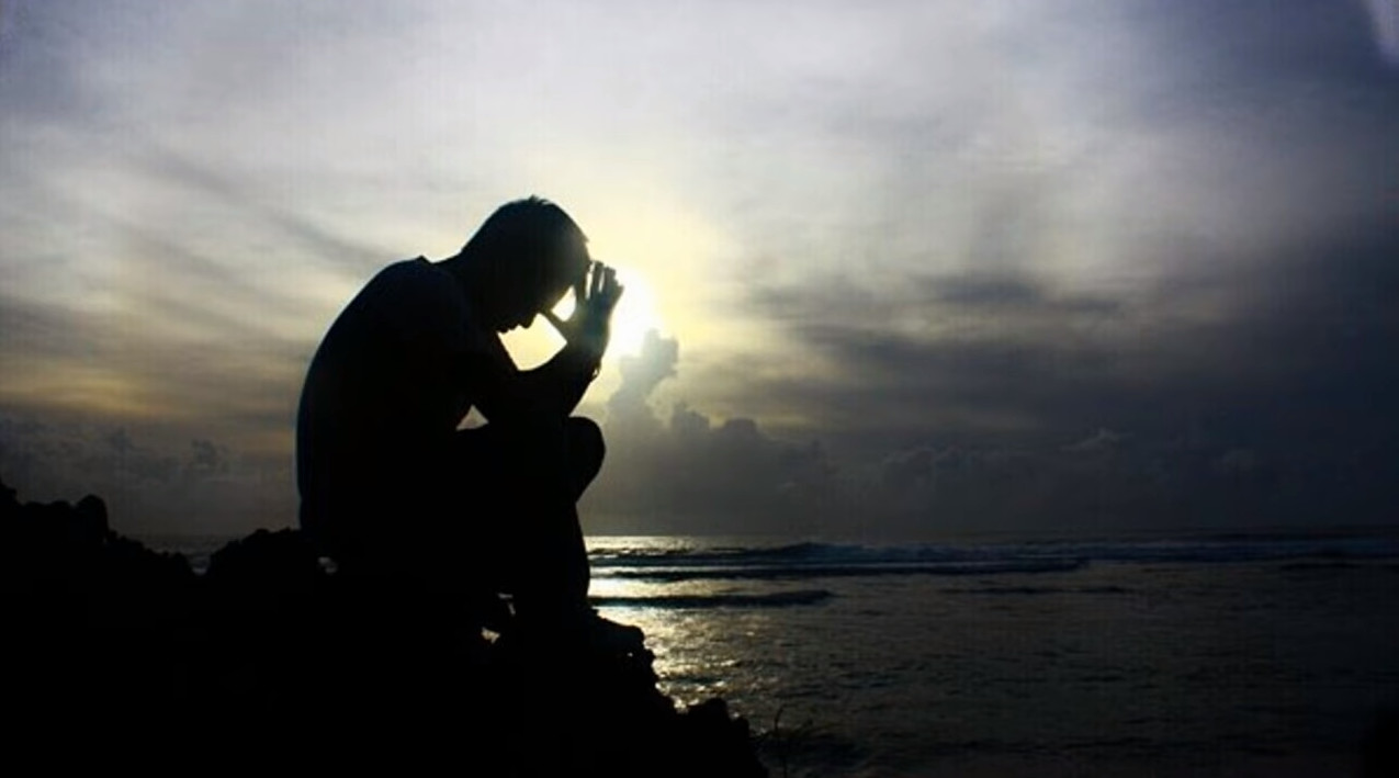 Man sitting on a rock by the ocean praying